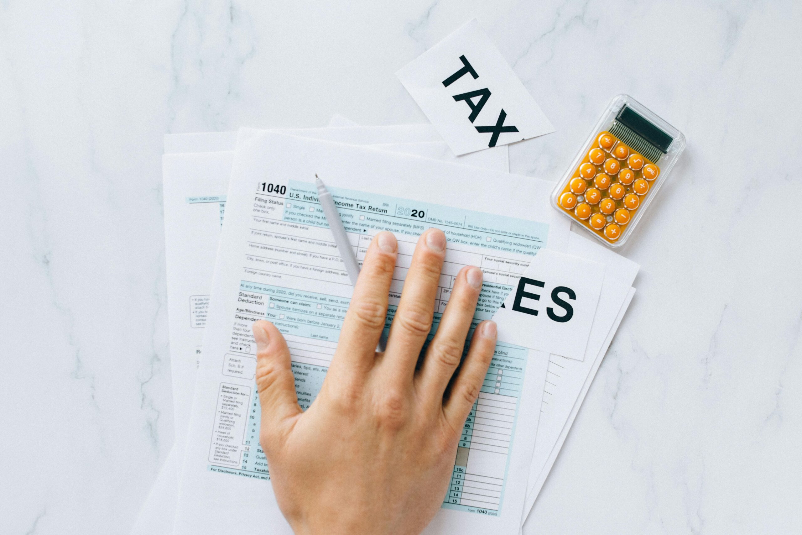 Close-up of a hand on tax form 1040 with a calculator on a desk.